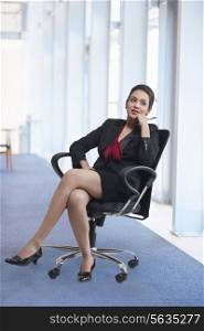 Full length of thoughtful businesswoman sitting in office