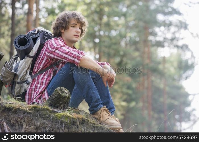 Full length of thoughtful male backpacker relaxing on cliff in forest