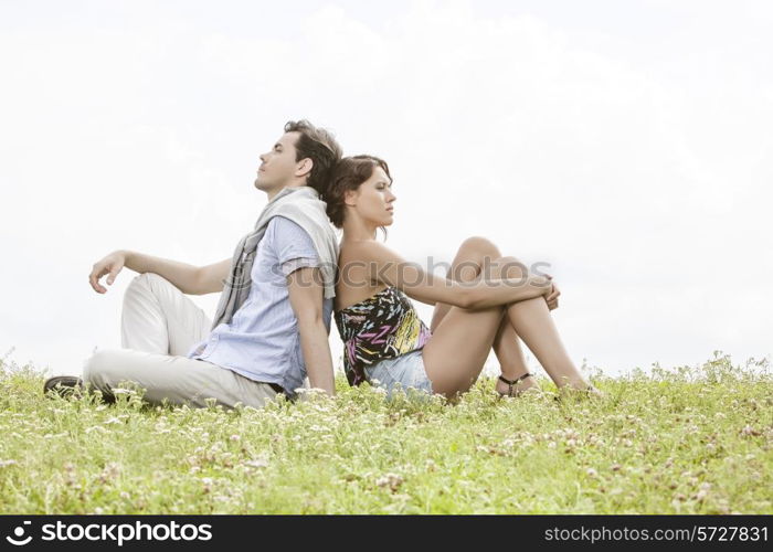 Full length of thoughtful young couple sitting back to back in park