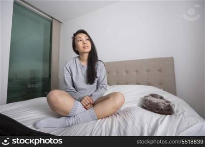 Full length of thoughtful young woman sitting on bed