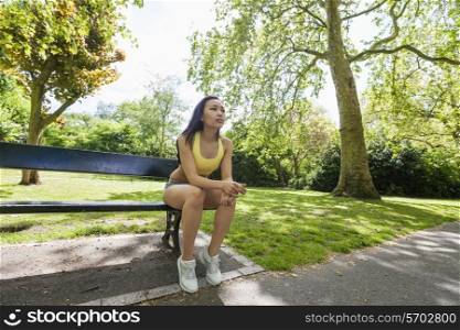Full length of tired fit woman sitting on beach while exercising in park
