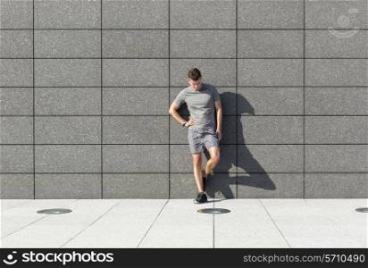 Full length of tired sporty man leaning on tiled wall