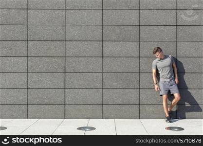 Full length of tired sporty man leaning on tiled wall