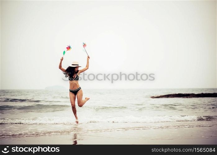 Full Length Of Woman Holding Pinwheel Toys While Jumping At Beach