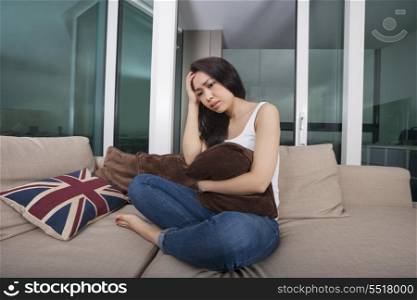 Full length of worried young woman sitting on sofa