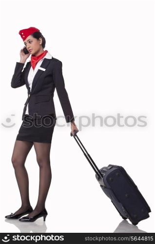 Full length of young airhostess on call while pulling luggage bag isolated over white background