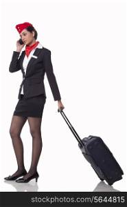 Full length of young airhostess on call while pulling luggage bag isolated over white background