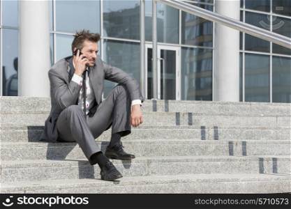 Full length of young businessman answering cell phone on steps outside office