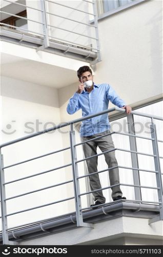 Full length of young businessman drinking coffee at hotel balcony