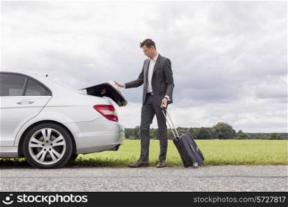 Full length of young businessman unloading luggage from broken down car at countryside