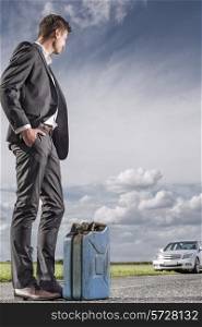 Full length of young businessman with petrol can looking at broken car at countryside