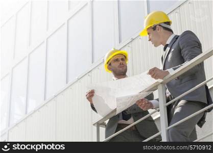 Full length of young businessmen discussing over blueprint on stairway