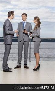 Full length of young businesspeople holding wineglasses while communicating on terrace