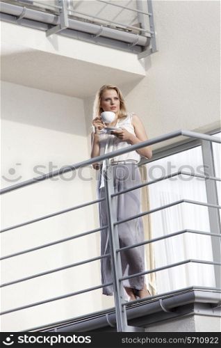 Full length of young businesswoman having coffee at hotel balcony