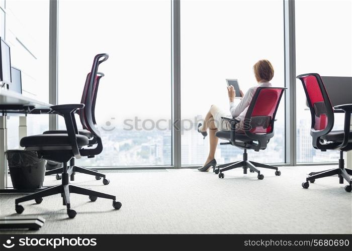 Full length of young businesswoman using tablet PC on chair in office