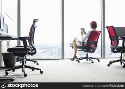 Full length of young businesswoman using tablet PC on chair in office