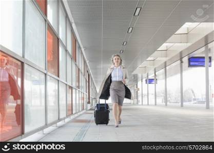 Full length of young businesswoman with luggage rushing in railroad station