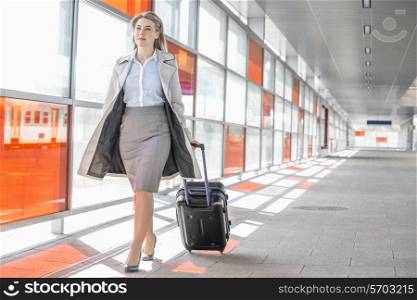 Full length of young businesswoman with luggage walking in railroad station
