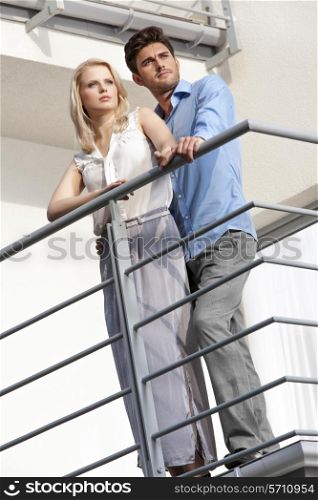 Full length of young couple looking away while standing at balcony