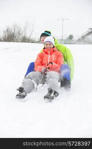 Full length of young couple sledging on snow covered land