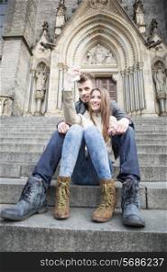 Full length of young couple taking selfie while sitting on steps outdoors