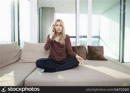 Full length of young displeased woman talking on mobile phone at home