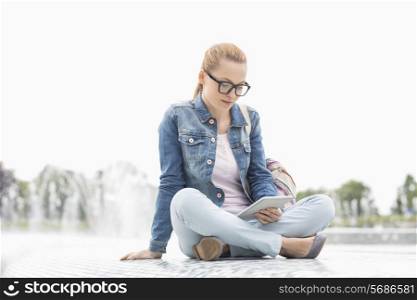 Full length of young female college student using digital tablet in park