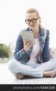 Full length of young female college student using tablet PC in park