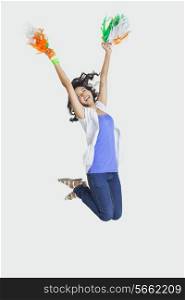 Full length of young female jumping in mid-air with Indian tricolor pom poms over white background