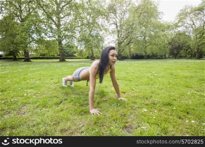 Full length of young fit woman performing pushups at park