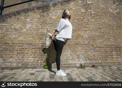 Full length of young fit woman stretching against brick wall