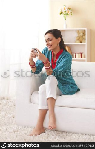 Full length of young Indian woman text messaging in living room