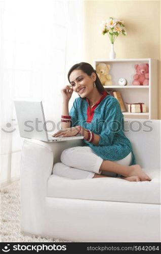 Full length of young Indian woman using laptop on sofa at home