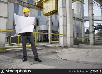 Full length of young male architect examining blueprint outside industry