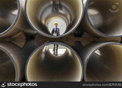 Full length of young male architect through stacked pipes at construction site