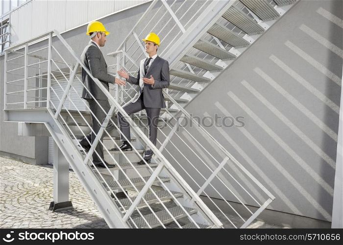 Full length of young male architects discussing on steps