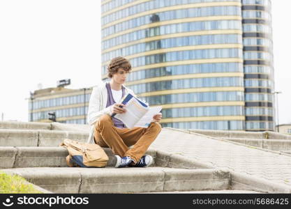 Full length of young male college student reading book against building