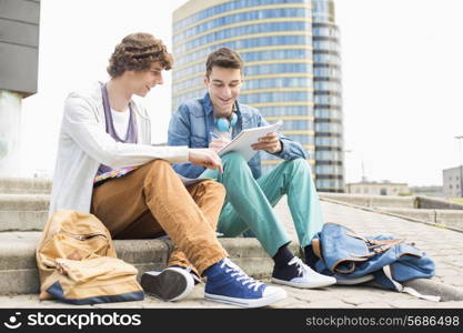 Full length of young male college students studying on steps against building