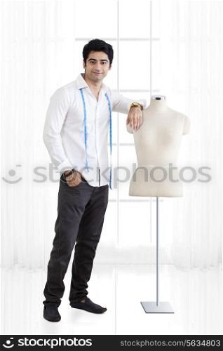 Full length of young male fashion designer standing by mannequin