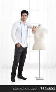 Full length of young male fashion designer standing by mannequin