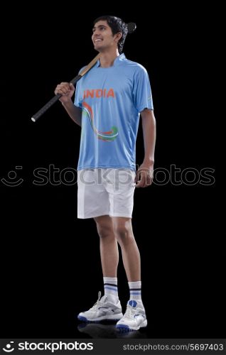 Full length of young male hockey player with stick standing against black background