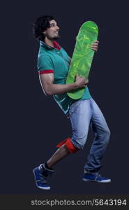 Full length of young man holding a skateboard like a guitar against black background