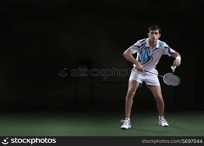 Full length of young man holding badminton racket and shuttlecock at court