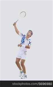 Full length of young man in sports wear playing badminton isolated over gray background