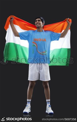 Full length of young man in sportswear holding Indian flag isolated over black background