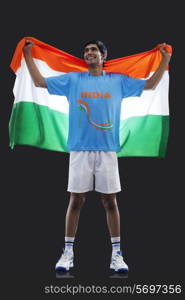 Full length of young man in sportswear holding Indian flag isolated over black background