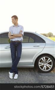 Full length of young man looking away while standing by car at countryside