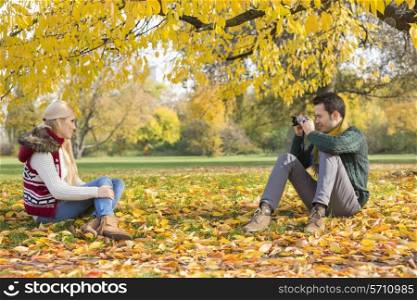 Full length of young man photographing woman in park during autumn
