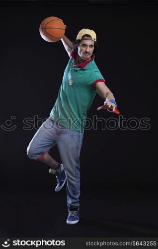 Full length of young man playing basket ball against black background
