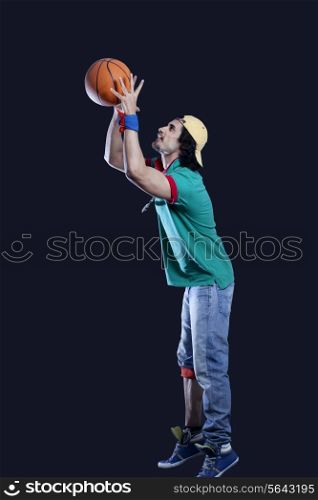 Full length of young man throwing basket ball against black background